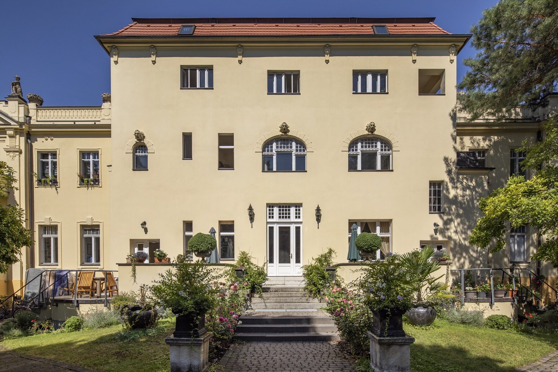 Das Löwenpalais von der Gartenseite: helle Villa mit Rundbogenfenstern, Freitreppe und blühendem Garten Das Löwenpalais von der Gartenseite: helle Villa mit Rundbogenfenstern, Freitreppe und blühendem Garten